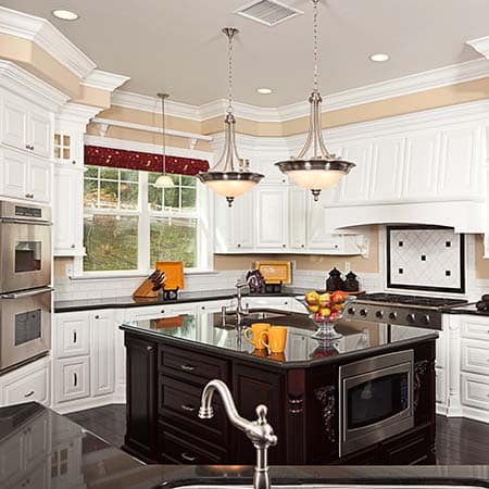 Elegant kitchen with white cabinetry, a dark wood island featuring a built-in microwave, stainless steel appliances, pendant lighting, and a large window above the sink.