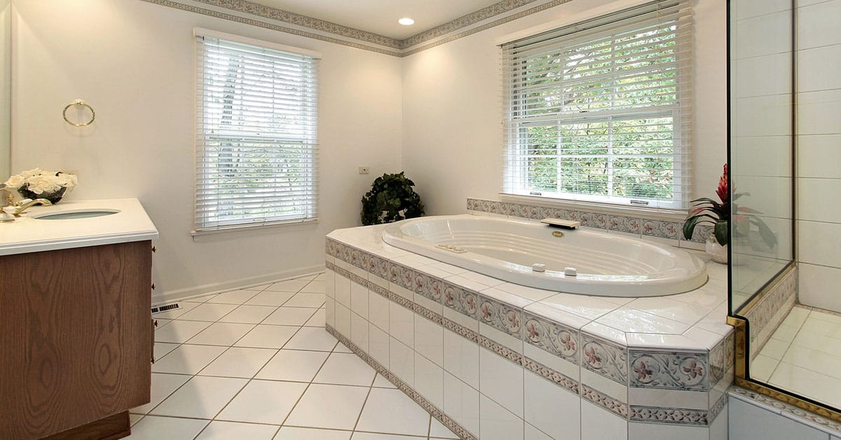 Bright bathroom with tiled drop-in tub, glass shower, white tile floor, two windows.