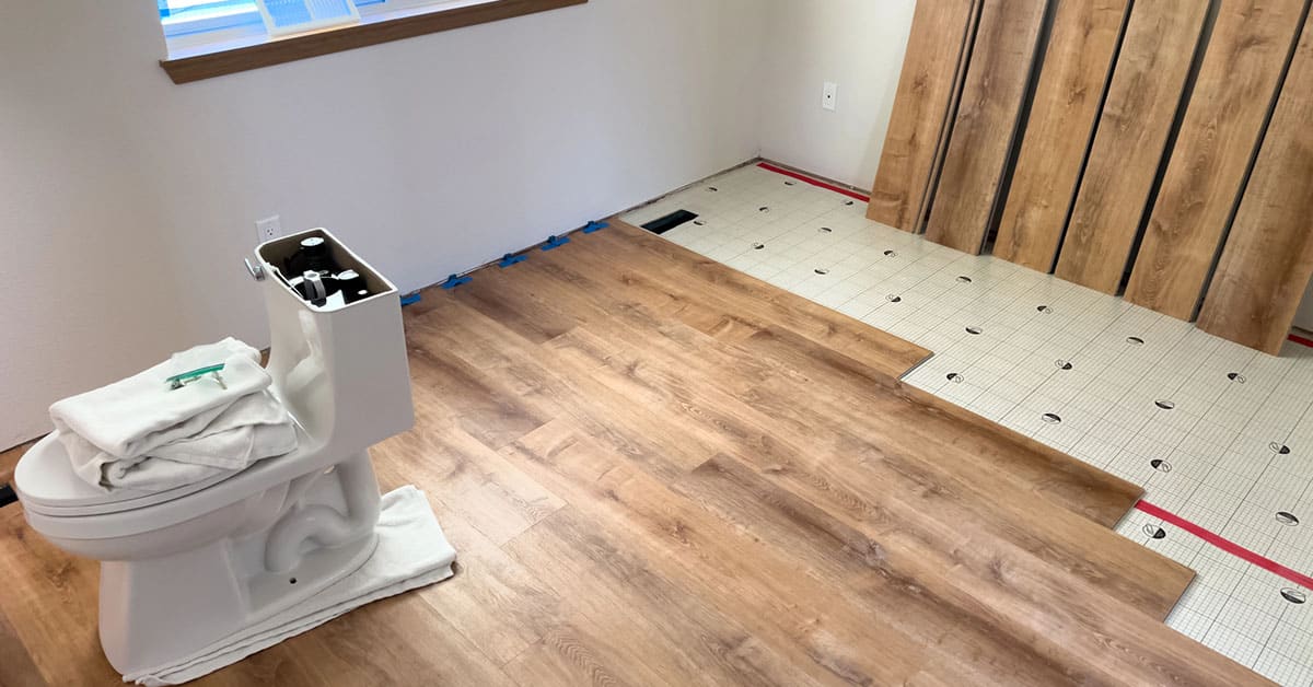 Bathroom remodel: laminate planks mid-install, toilet disconnected and set on towels.